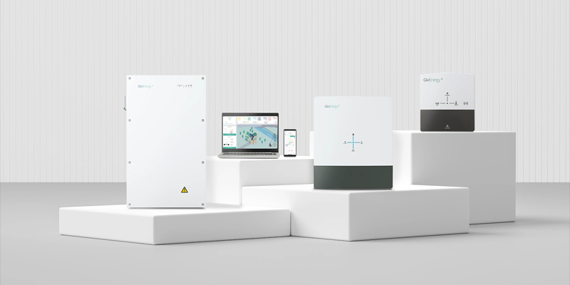 GivEnergy solar inverter and battery system range displayed on white plinths alongside monitoring app on laptop and smartphone